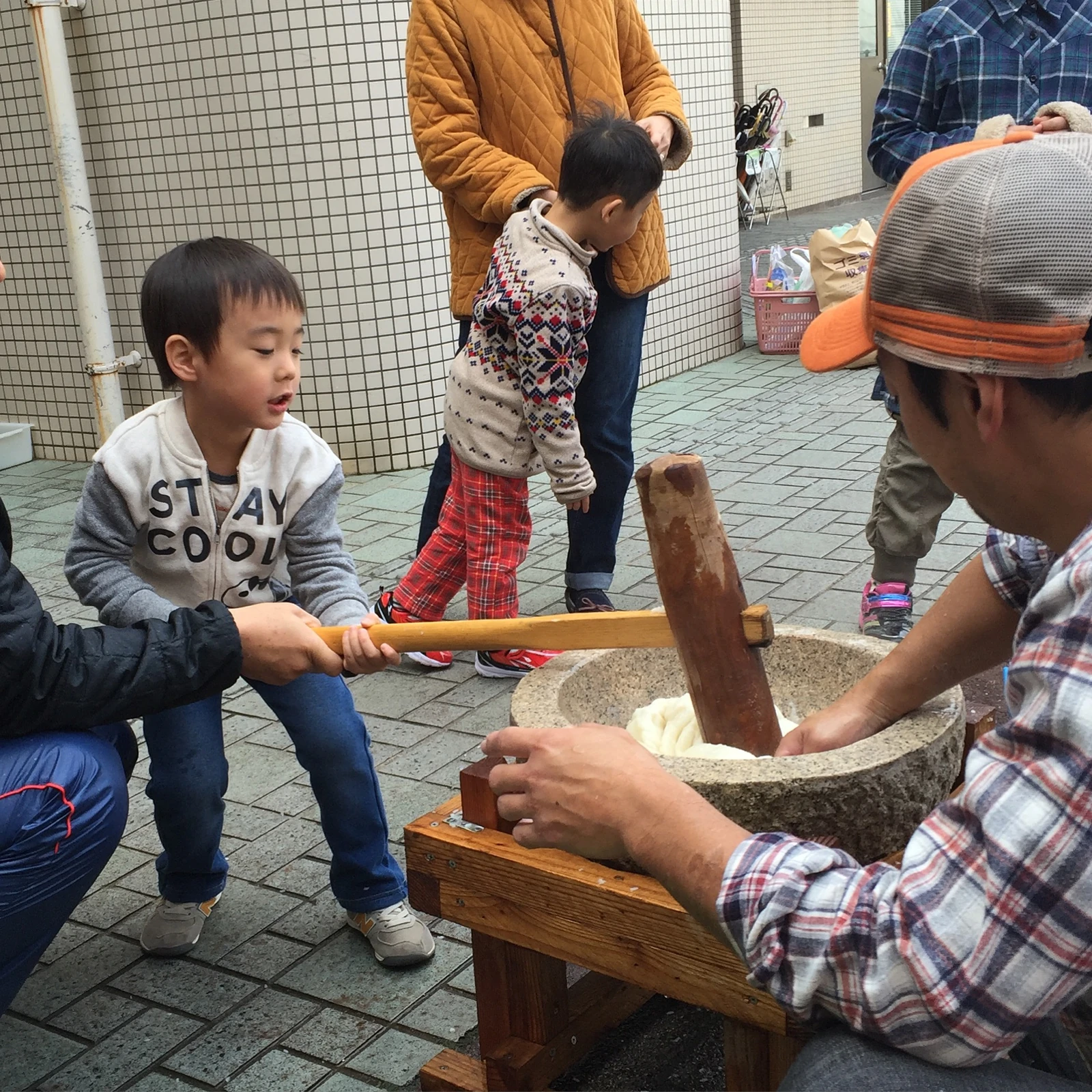 大人に手伝ってもらいながら杵を持ち、餅つきを楽しむ子ども